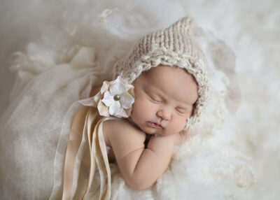 A baby sleeping in a knitted hat on a white blanket.