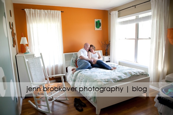A couple captured by Jenn Brookover Photography sitting on a bed in an orange bedroom.