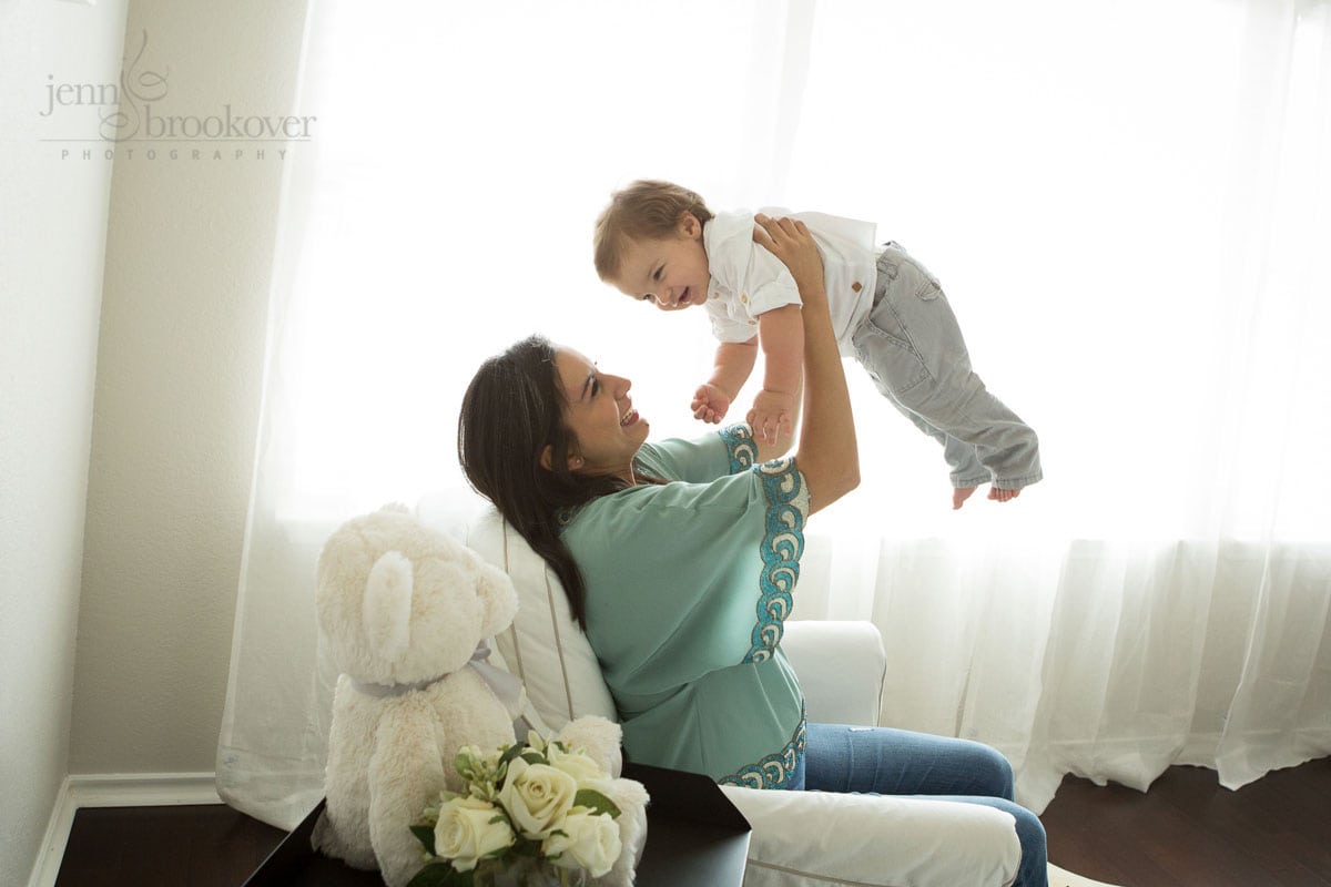 mom holding toddler up in window light