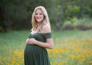 A pregnant woman in a green dress standing in a field of yellow flowers.