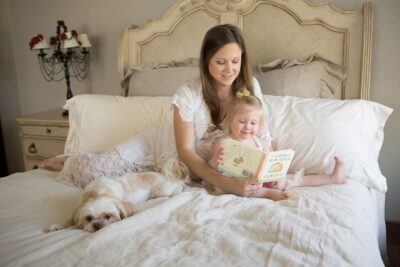 A woman reading a book to her baby on a bed.