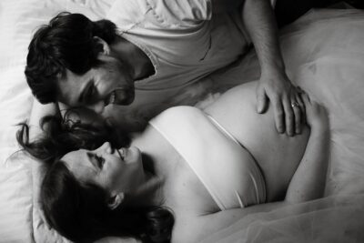 A pregnant woman laying on a bed with her husband.