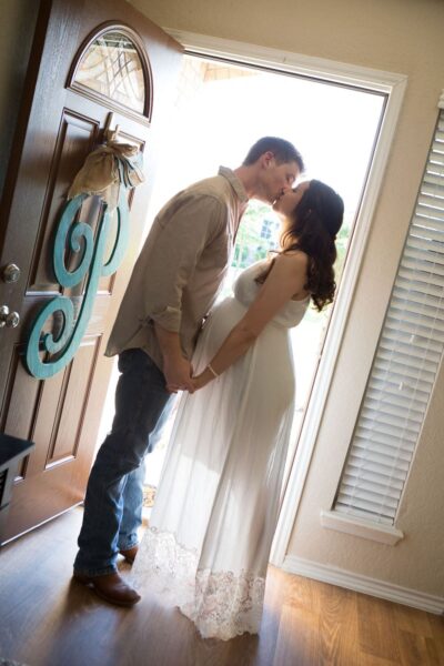 A pregnant couple kissing in front of a door.