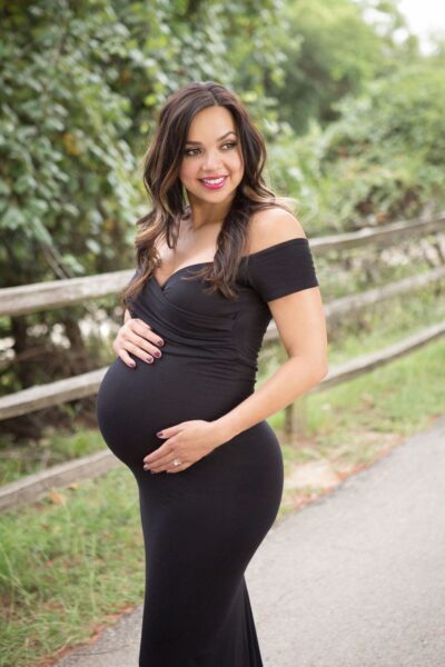 A pregnant woman in a black dress poses for a photo.