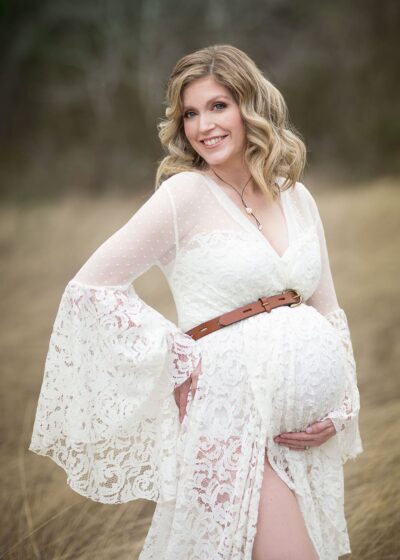 A pregnant woman in a white dress poses in a field.