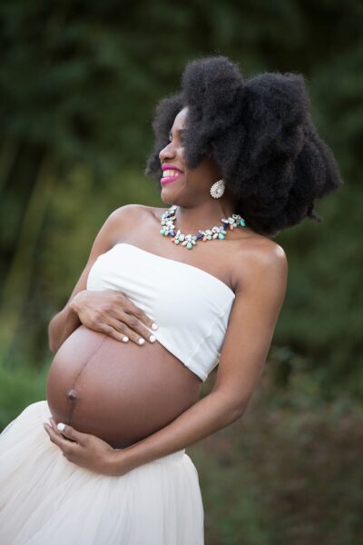 A pregnant woman in a white dress with afro hair.