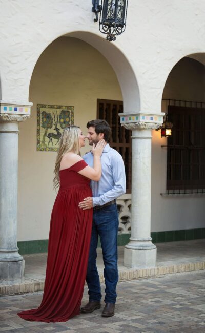 A couple in a red dress kisses in front of an archway.