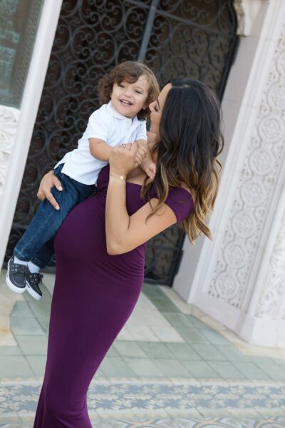 A pregnant woman holding her son in a purple dress.