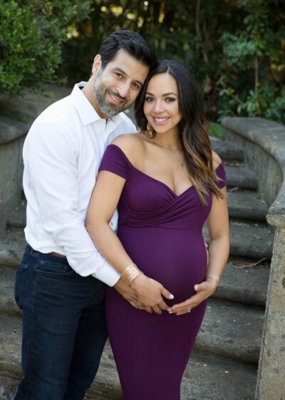 A man and woman pose for a maternity photo in a purple dress.