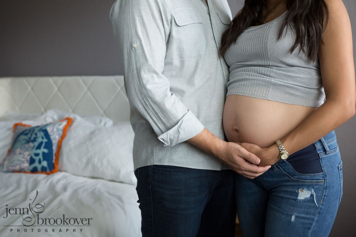 dad and mom holding hands in master bedroom for maternity session portrait
