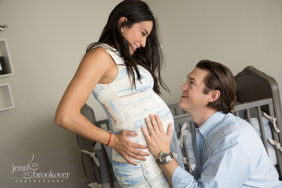 couple in nursery smiling and hugging belly during maternity photo session at home