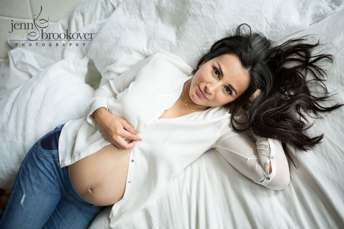 mom on white bed during her maternity photo session