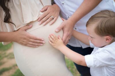 A pregnant woman is holding a child's hand.
