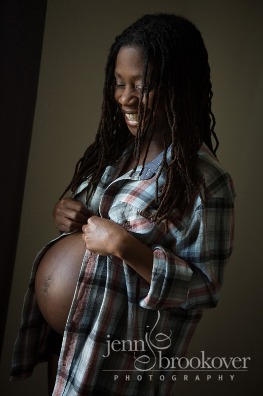 pregnant mom dressed in dad's plaid shirt smiling and looking at belly during maternity photo session by Jenn Brookover Photography