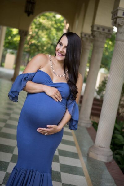 A pregnant woman in a blue dress poses for a photo.