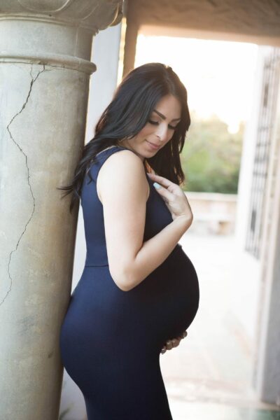 A pregnant woman in a black dress leaning against a column.