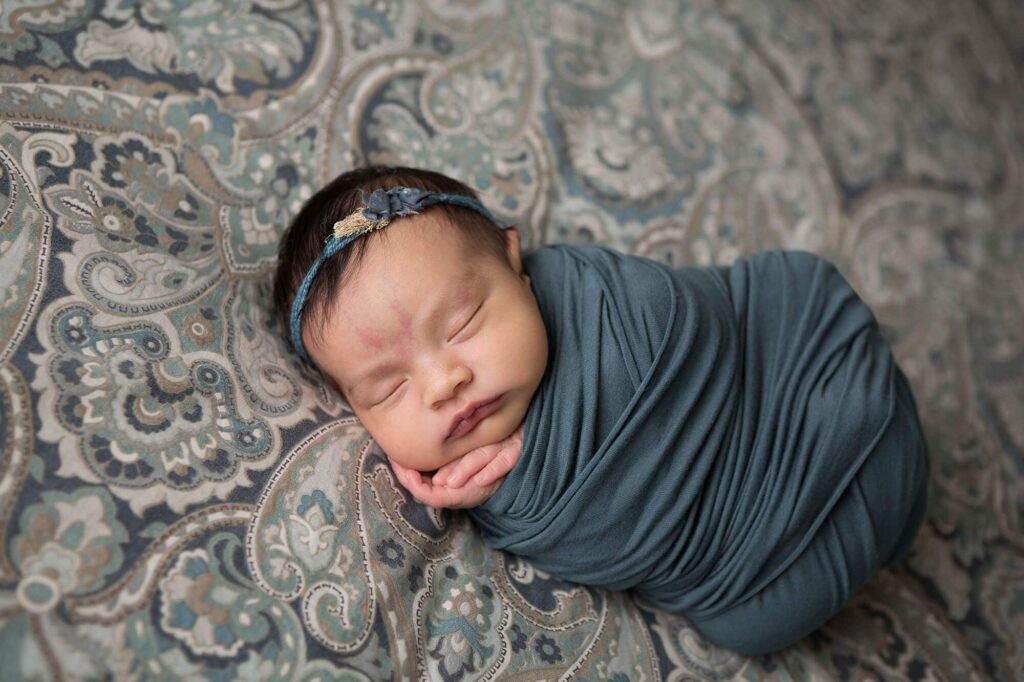 newborn wrapped in teal on bed at home newborn photo session