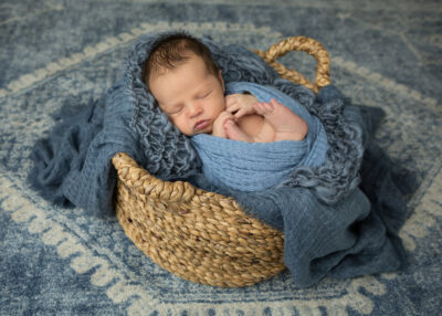 A baby boy sleeping in a basket on a rug.