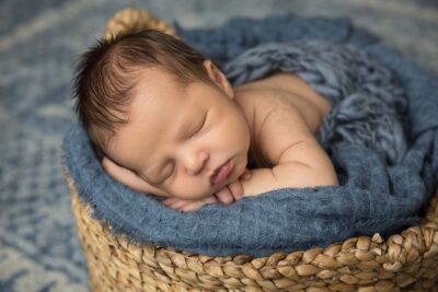 A baby boy sleeping in a basket.
