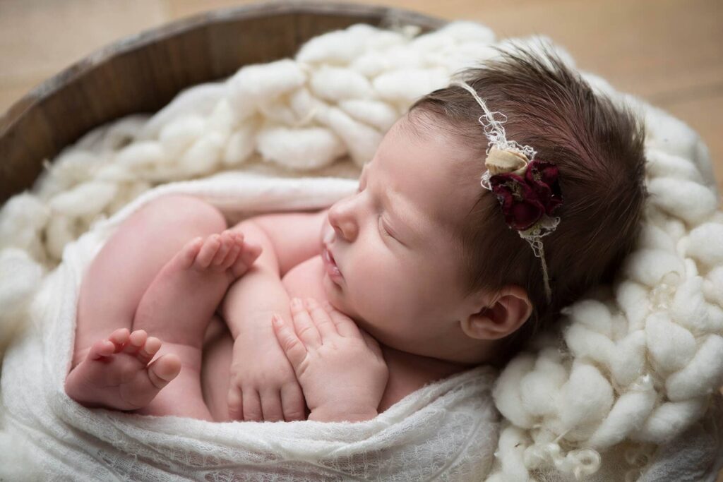 A baby girl sleeping in a basket with a flower headband.