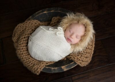 A newborn baby sleeping in a bowl on a wooden floor.
