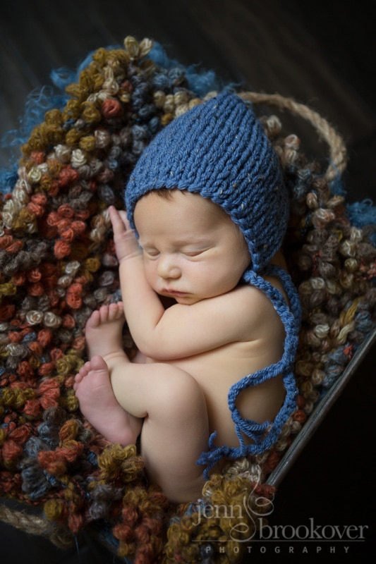 newborn portrait in a blue hat on orange, blue and brown blanket