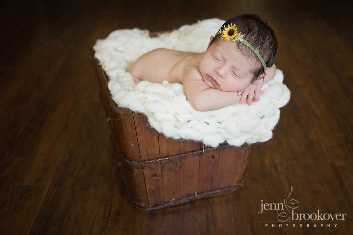 newborn in a bucket with a sunflower headband on wood floor