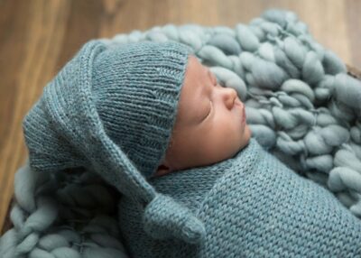 A newborn sleeping in a blue knitted hat.