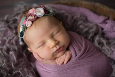 A newborn sleeping in a basket with a flower headband.