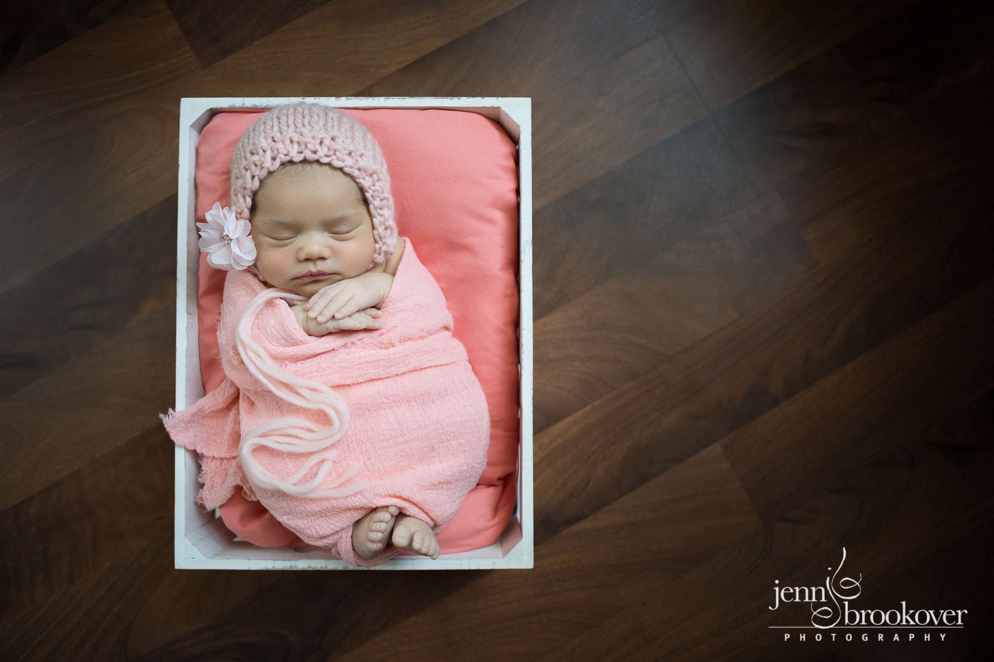 newborn wrapped in peach and coral in a white basket on a wood floor by Jenn Brookover Photography in San Antonio