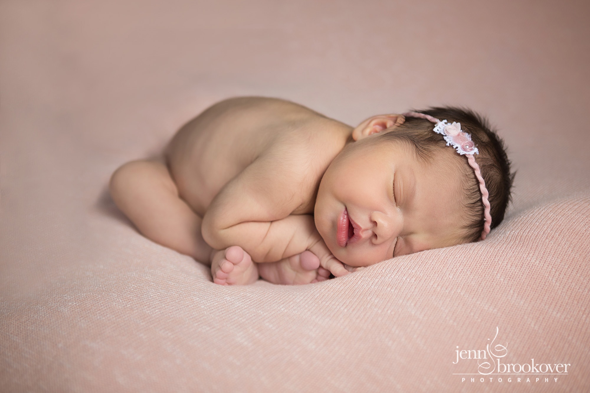 newborn curled up on peach, headband by Devoted Knits taken by Jenn Brookover in San Antonio