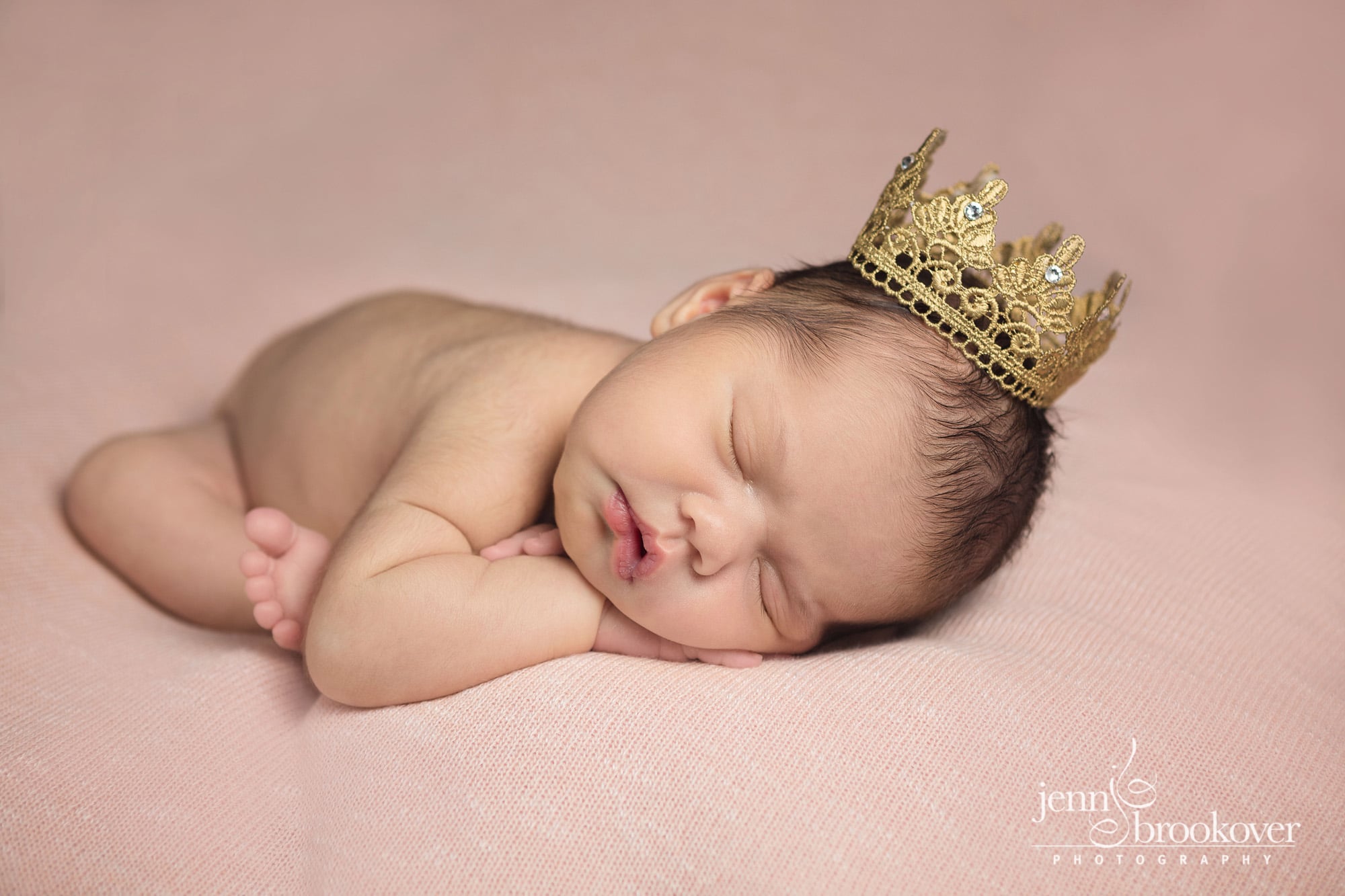 baby girl with a gold crown on with pink background taken by Jenn Brookover in San Antonio Texas