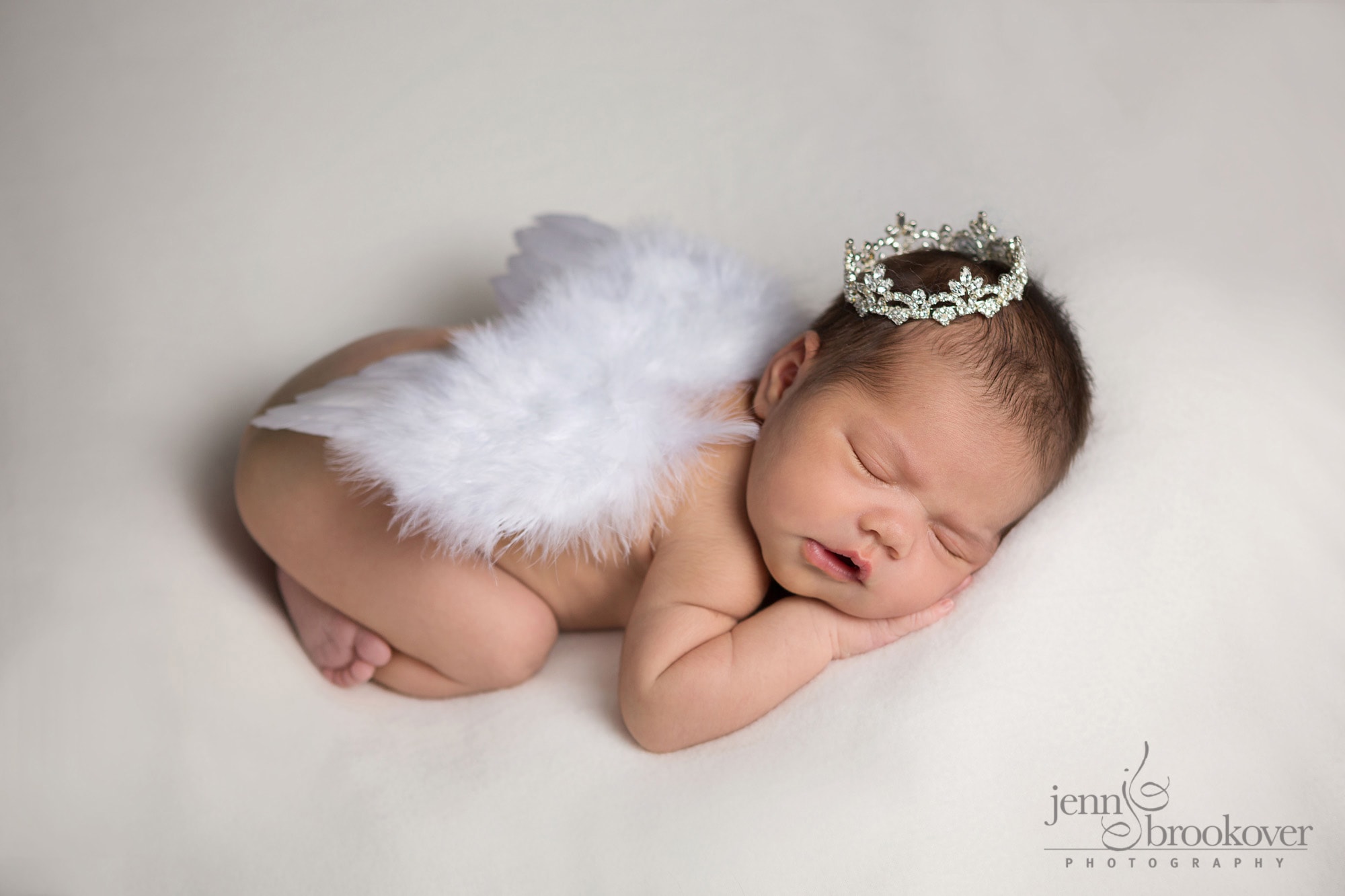 newborn with wings and crown sleeping on white background during her photo shoot with Jenn Brookover Photography in San Antonio