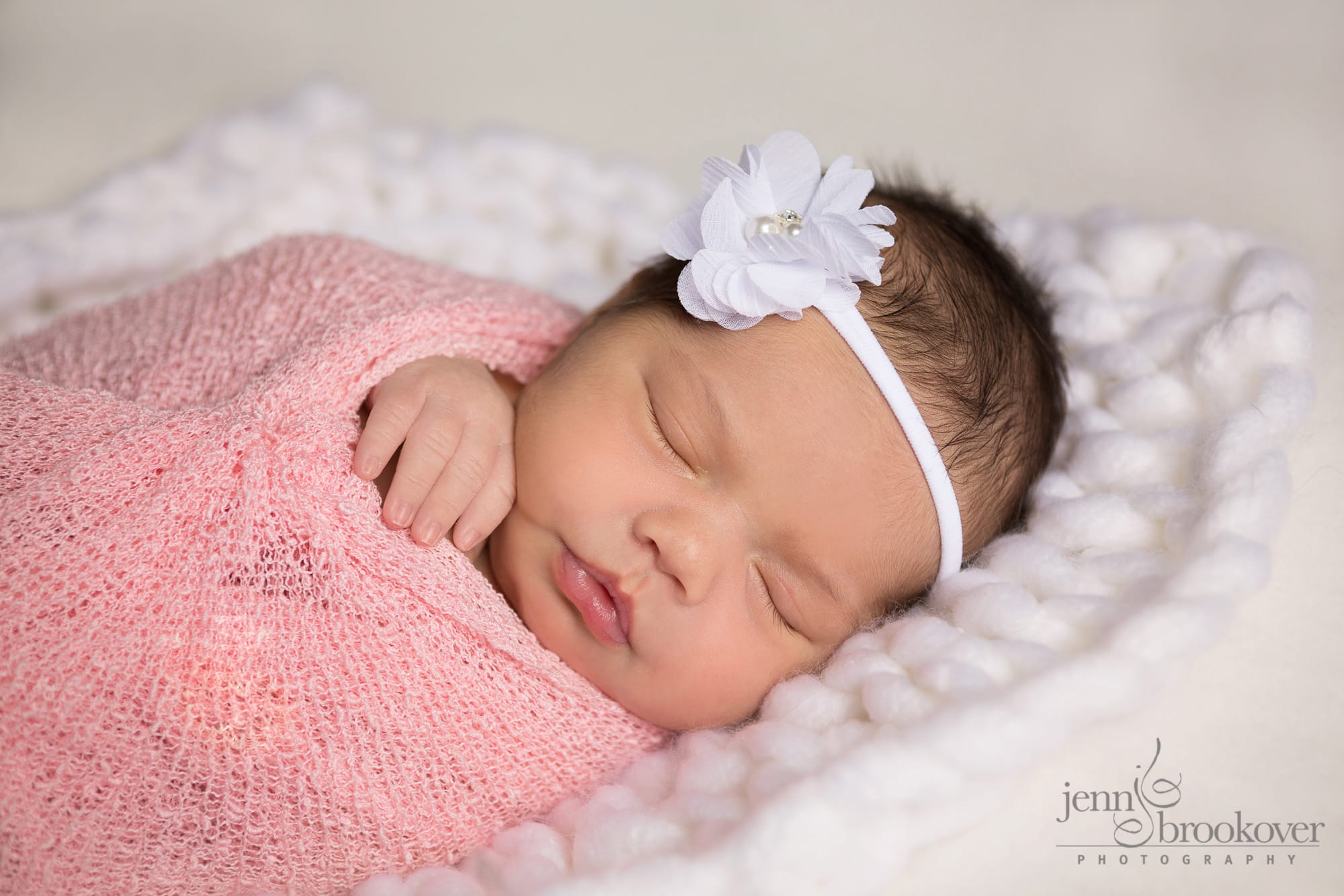 newborn wrapped in pink with white flower headband during her photo shoot with Jenn Brookover in San Antonio