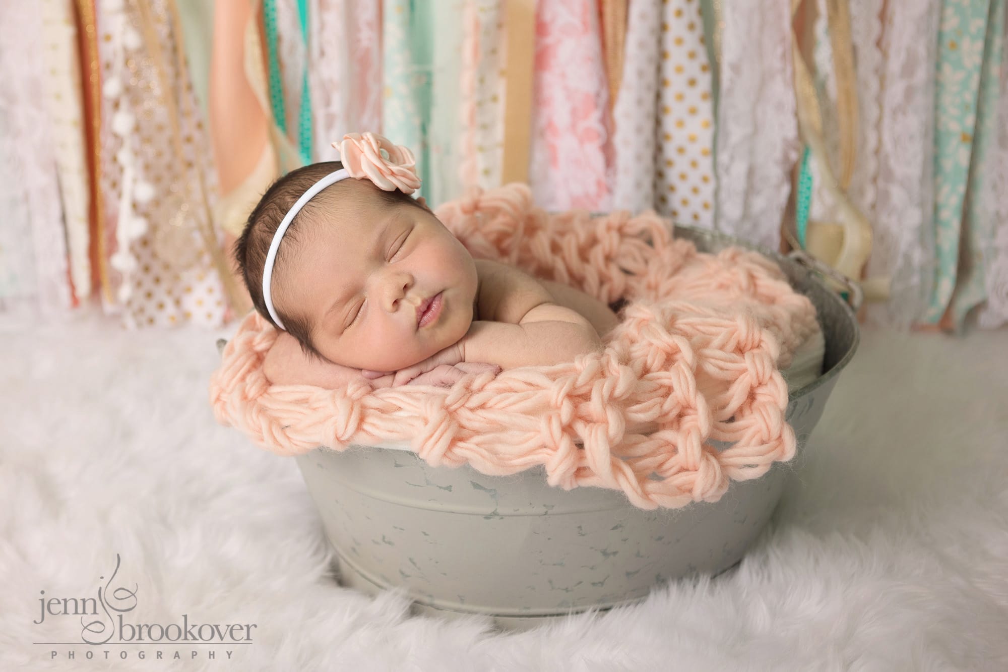 A baby girl is sleeping in a bucket with a pink bow.