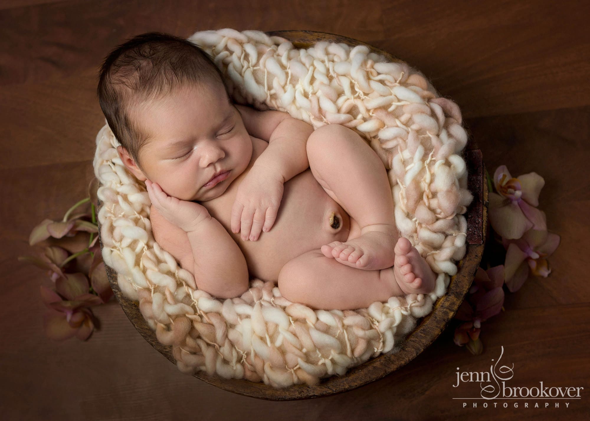 newborn in peach with flowers cuddled up for her newborn portrait session with Jenn Brookover in San Antonio