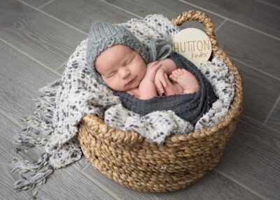A baby boy sleeping in a basket on a wooden floor.