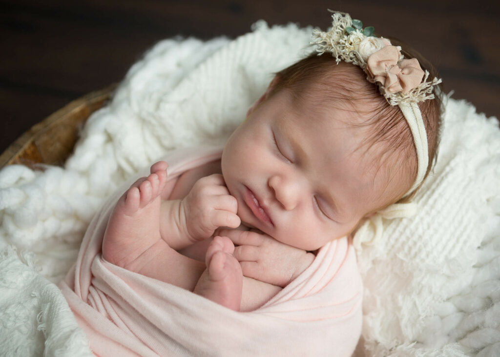 A baby girl sleeping in a basket with a flower headband.