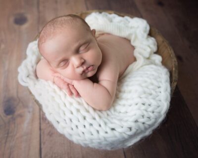 A newborn baby sleeping in a white knitted basket.