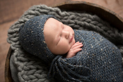 A newborn sleeping in a knitted hat in a wooden bowl.