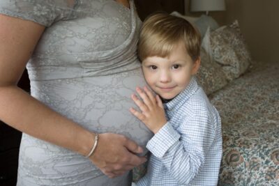 A pregnant woman posing with her son on a bed.