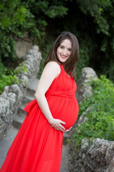 A pregnant woman in a red dress is posing for a photo.