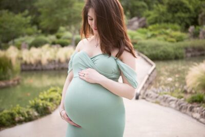 A pregnant woman in a green dress is posing in a park.