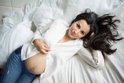 A pregnant woman laying on a white bed.