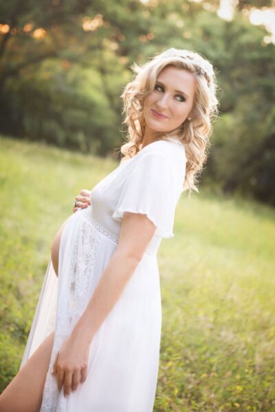 A pregnant woman in a white dress posing in a field.