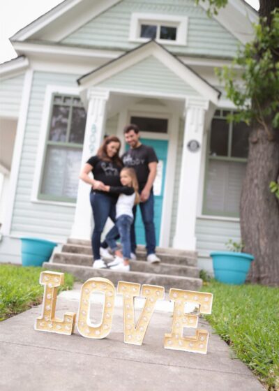 A family is posing in front of a house with a love sign.