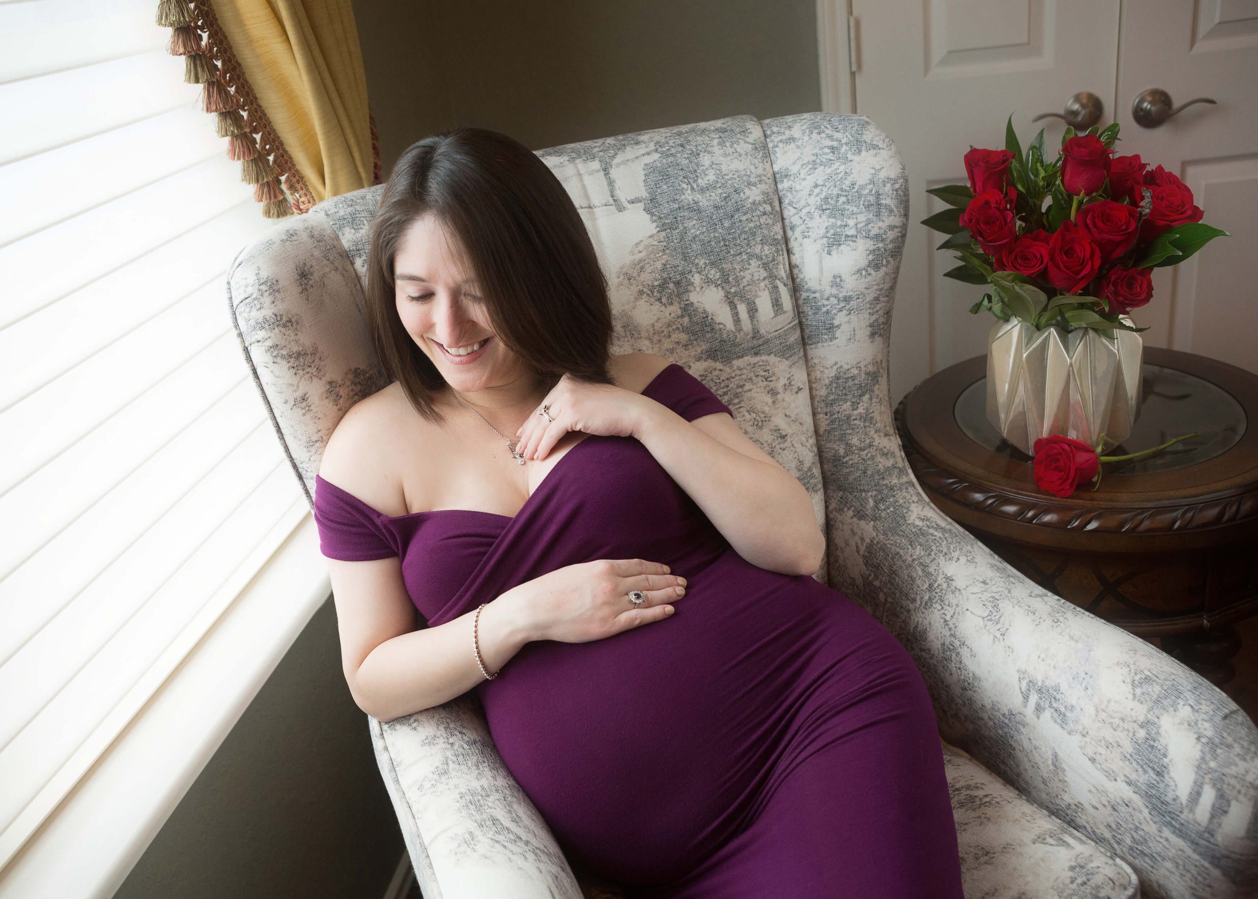 A pregnant woman in a purple dress sitting in a chair.