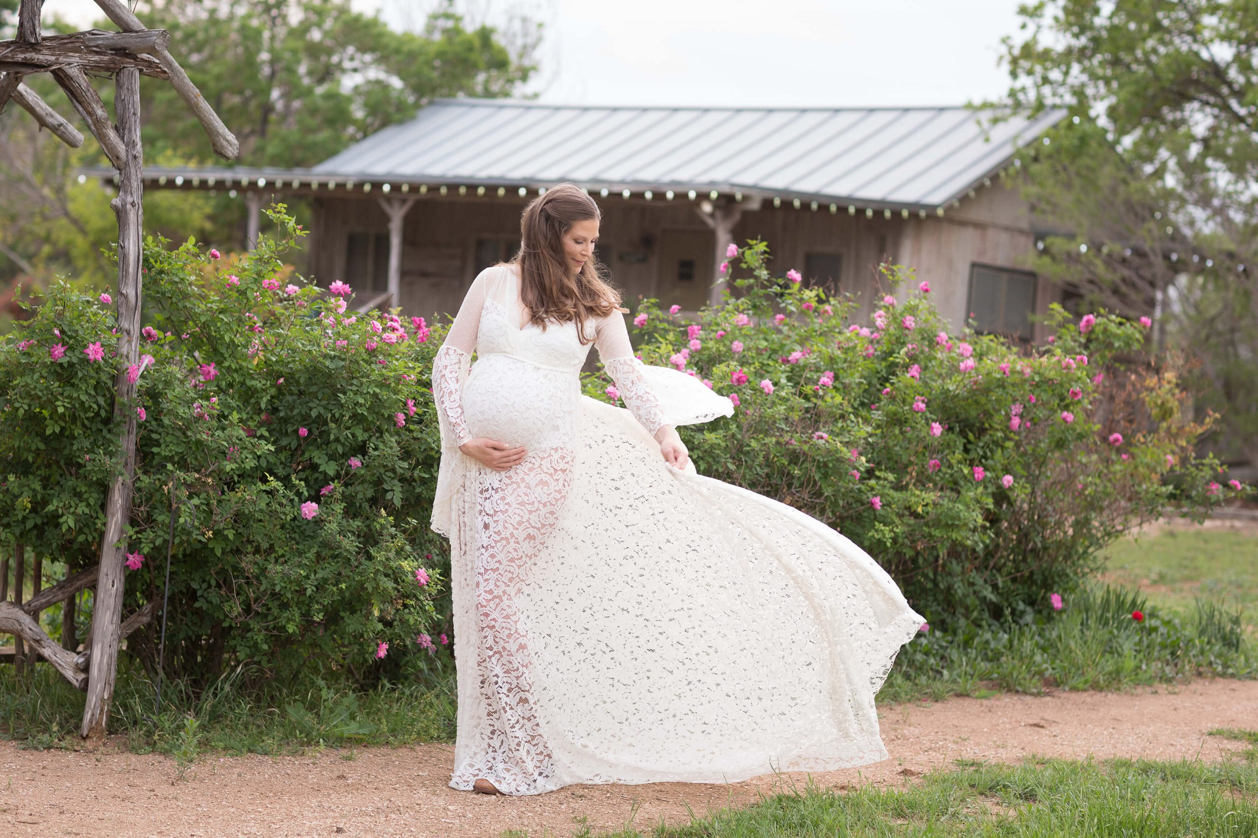 A pregnant woman in a white dress standing in front of a house.