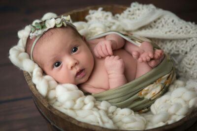 A baby girl laying in a basket with a flower headband.