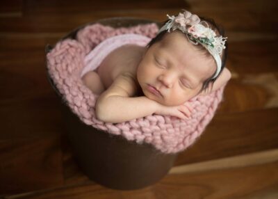 A newborn sleeping in a bucket on a wooden floor.